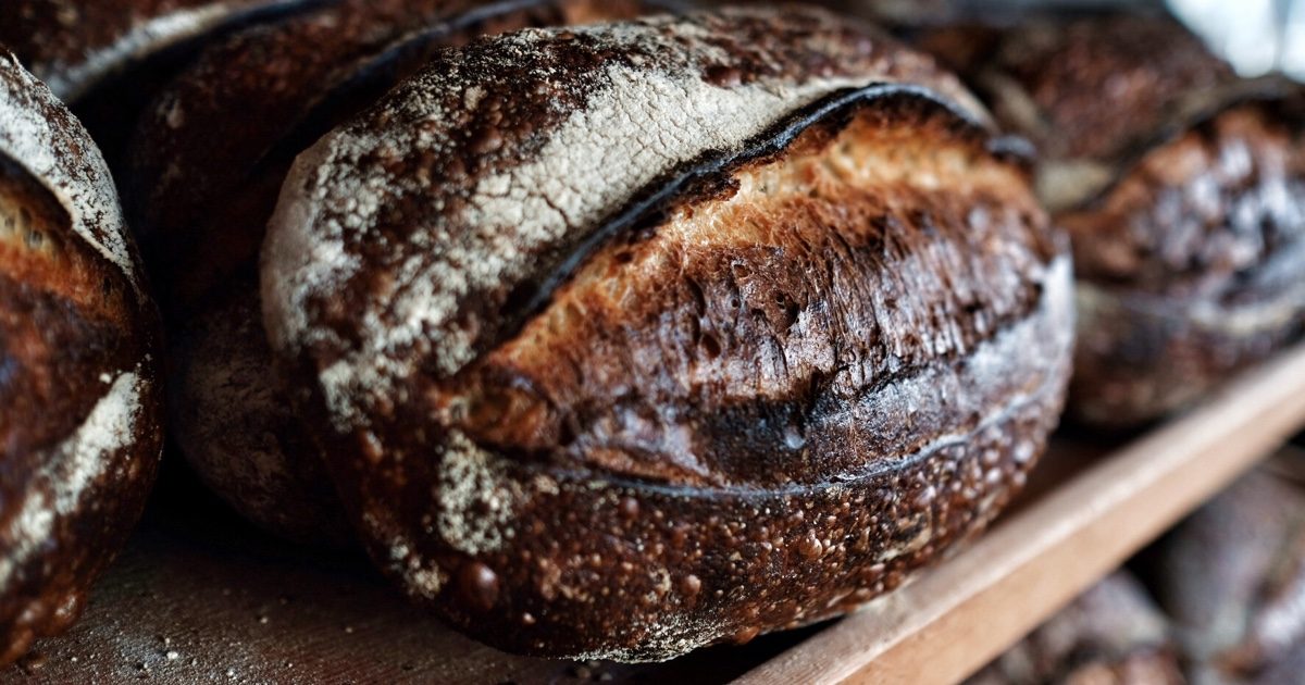Burnished Tartine country loaves stacked on a wooden shelf